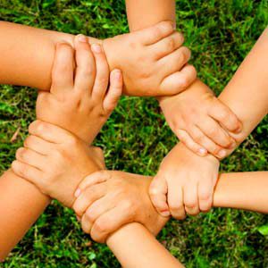 Four little kid hands holding on to each other and creating a team circle.