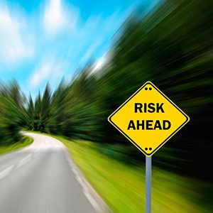 Road surrounded by trees blending together as a risk ahead sign shows up.