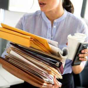 A young business woman balancing too many papers in her hands.