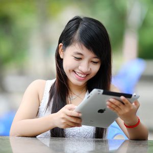 Young millennial girl looking down at her ipad and smiling at the information she is reading.