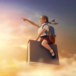 A little girl is flying with a book to her new destination and is pointing at the place that she is intending to arrive.