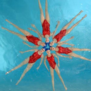 Team of synchronized swimmers performing a dance arranged in a circle.