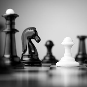 Black and white chess pieces with one white piece standing tall in front of them all.